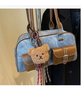 Detail of denim Boston bag with leather straps and plush bear charm hanging on handle