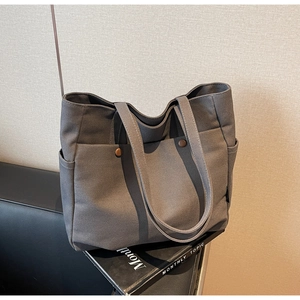 Close-up of grey canvas tote bag with brown button pocket and side compartments