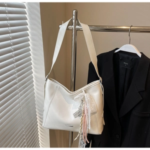 Detail of white half-moon shoulder bag with lace bow charm and metal logo on strap