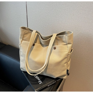 Detail of beige canvas tote bag showing side pocket and woven label on a leather sofa