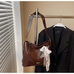 Detail of brown leather bucket bag with white lace bow and metal tennis racket charm