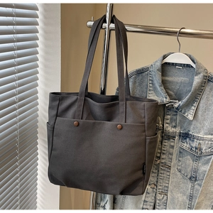 Detail of dark grey canvas tote bag featuring reinforced rivets and side pockets on display
