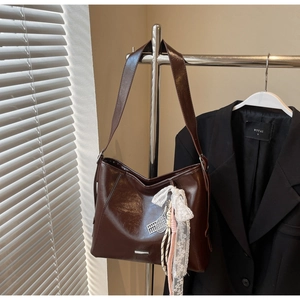 Detail of dark brown glossy shoulder bag with lace bow and tennis racket charm