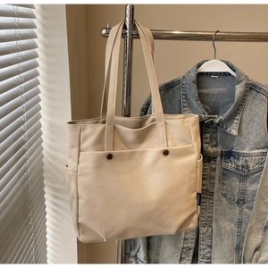 Detailed close-up of beige canvas tote bag with front pocket and dark brown buttons