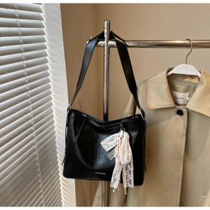 Detail of black faux leather tote bag with elegant white lace bow and wide shoulder strap