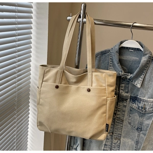 Detail view of beige canvas tote bag showing front pocket with decorative buttons