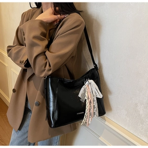 Detail of minimalist black bucket bag with vintage lace pendant and glossy leather texture