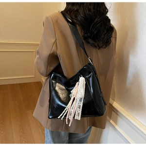 Detail of glossy black shoulder bag with decorative white lace and pink ribbon pendant