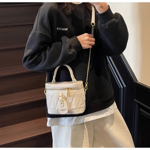 Detail einer weißen Beuteltasche mit V-Nähten und einem goldenen Kettenriemen