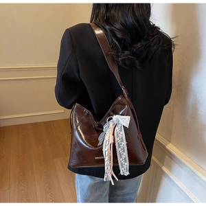 Detail of dark brown leather bucket bag featuring decorative lace and tassel charms