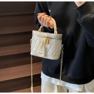 Detail der cremeweißen gesteppten Beuteltasche mit Goldkette und Lederanhänger