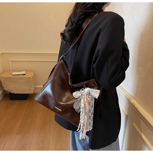 Detail of a dark brown glossy leather bucket bag with silver trim and lace bow