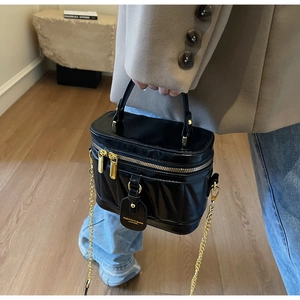 Detail einer schwarzen gesteppten Beuteltasche mit Goldkette und Lederanhänger