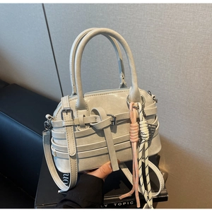 Detail of grey leather handbag featuring cross straps and a knitted braided lanyard