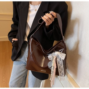 Detail of dark brown glossy leather bucket bag with lace bow and tennis racket charm