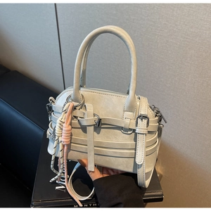 Close-up of a light gray handbag with decorative straps and silver buckles detail