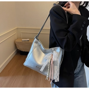 Silver faux leather bucket bag shown on shoulder with lace and pink woven charm details