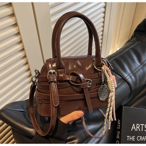 Detail of caramel brown glossy handbag with decorative straps and tennis racket pendant