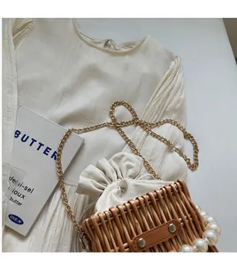 Detail of woven straw bucket bag featuring a pearl handle and a fine gold chain strap