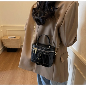 Modell mit schwarzer Lackleder-Eimertasche mit goldener Kette und Crossbody-Tragevariante