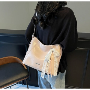 Detail of light pink shoulder bag featuring a lace bow pendant and woven tassel accents