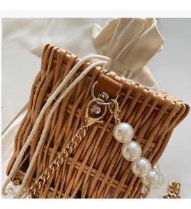 Close-up of woven straw bucket bag with pearl chain strap and drawstring closure