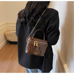 Detailansicht einer dunkelbraunen Stepptasche mit goldener Kette an einem Model von hinten