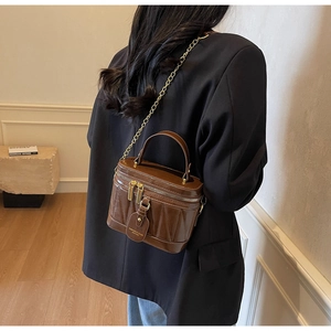 Detail der braunen gesteppten Lackleder-Eimertasche mit Goldkette und Tragegriff