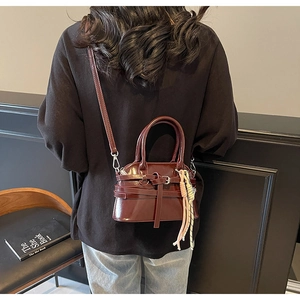 Detail of dark red leather shell bag with metallic buckle and woven tassel accessory