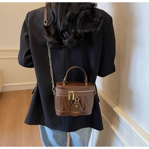 Nahaufnahme einer braunen gesteppten Kosmetiktasche mit Metallkette, getragen von Model