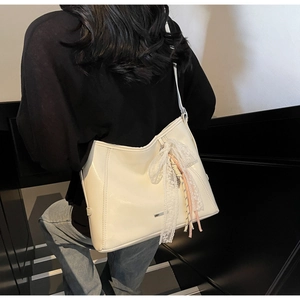Detail of off-white bucket bag with lace bow and charms shown on a shoulder