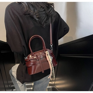 Detail view of burgundy shell bag with leather strap and woven tassel charm accents