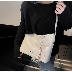 Close-up of white glossy shoulder bag featuring lace bow and colorful tassel detail