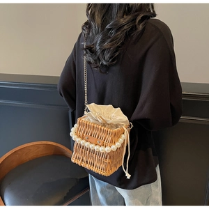 Detail of woven straw bucket bag featuring a pearl handle and drawstring inner pouch