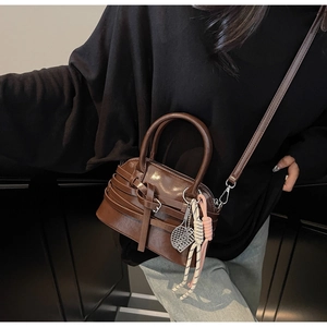 Detail view of deep brown shell bag with woven buckle and tennis racket charm