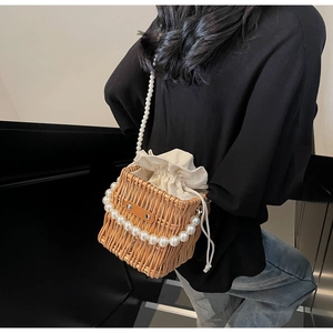 Detail of hand-woven straw bucket bag with elegant pearl strap and canvas drawstring liner