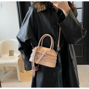 Macro shot of light pink glossy shell bag with woven belt detail and long tassel charm