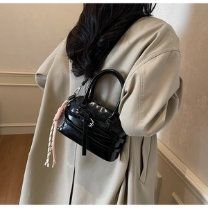 Detail of black shell handbag with buckles and pink braided tassel charm on trench coat