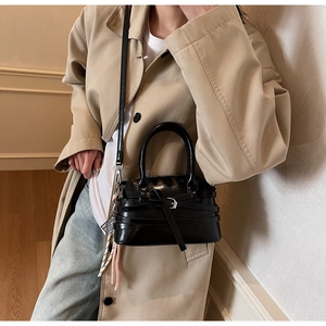 Detail of glossy black shell bag with metal buckles and decorative woven cord accessory