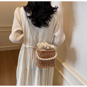 Detail of straw woven bucket bag featuring pearl handle and gold chain strap