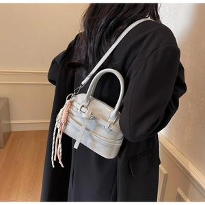 Detail of light gray crossbody shell bag with decorative pink and white woven tassel