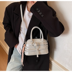 Detail of light gray crossbody bag with strap and pink tassel on a black blazer