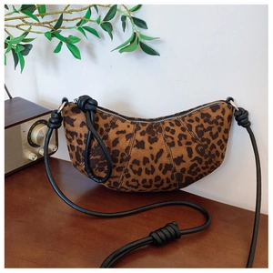 Detailed view of leopard print crescent bag with black knotted strap on a rustic table