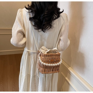 Detail of woven straw bucket bag featuring elegant pearl chain handle and drawstring lining