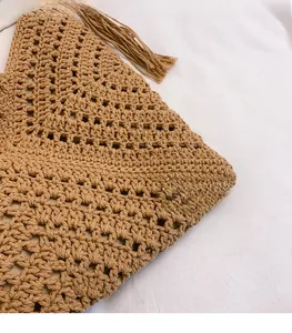 Detail of tan handmade woven tote with hollow-out crochet pattern and fringe tassels
