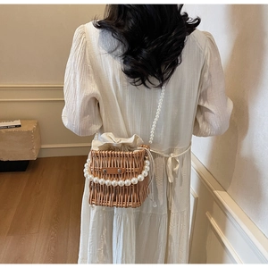 Detail of woven straw bucket bag with pearl chain handle and drawstring lining worn by model