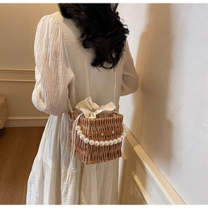 Detail of hand-woven straw bucket bag featuring a large pearl handle and drawstring pouch