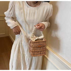 Detail of hand-woven straw bucket bag with large white pearls and brown leather clasp