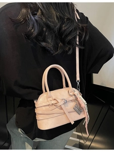Pink shell handbag with plaid scarf and silver charm shown on model in a dark setting