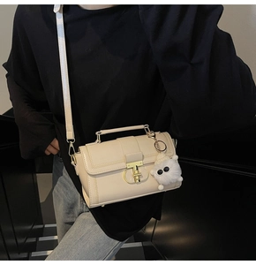 Κοντινό πλάνο κρεμ δερμάτινης τσάντας με καπιτονέ υφή και χρυσό μεταλλικό κλείδωμα T